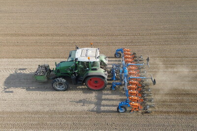 Hacktechnikeinsatz im Öko-Maisbestand - © Volker Graß Traktor pflügt ein großes Feld, zieht ein blau-orangefarbenes Pfluggerät hinter sich her.